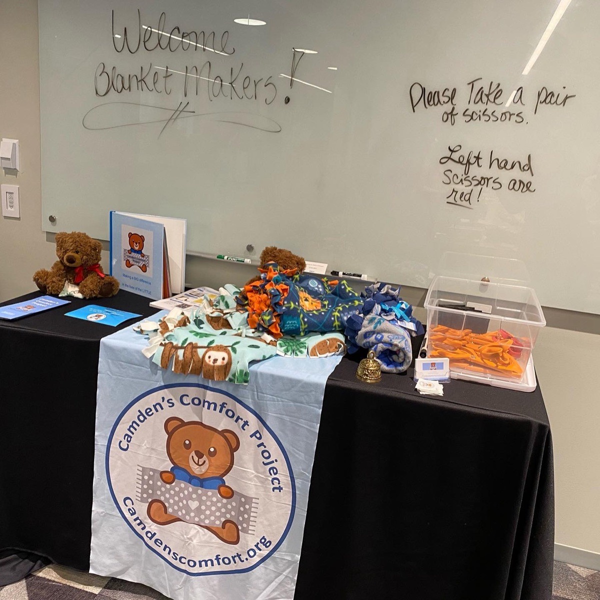 A blanket-making table set up with fleece, scissors, and a Camden's Comfort banner