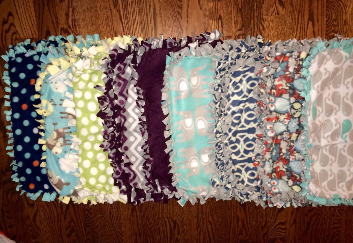 A row of finished no-sew fleece blankets on a wood floor